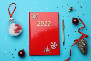 Photo of Red planner and Christmas decor on light blue background, flat lay. Planning for 2022 New Year