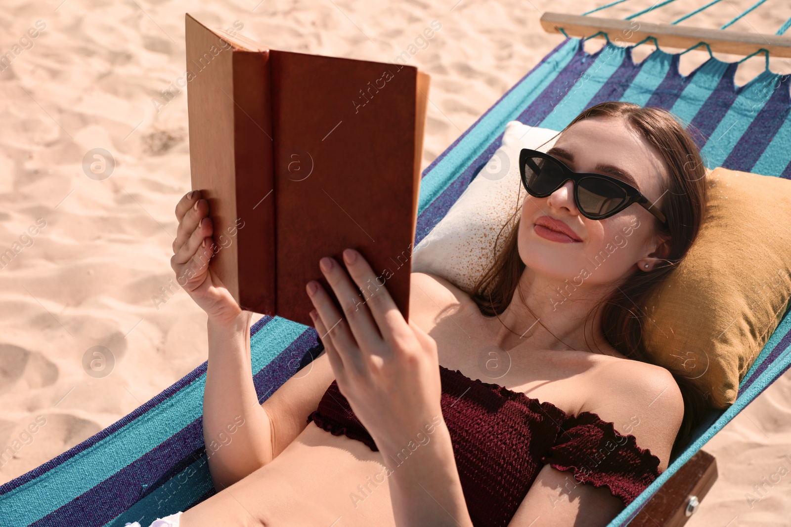 Photo of Young woman reading book in hammock on beach