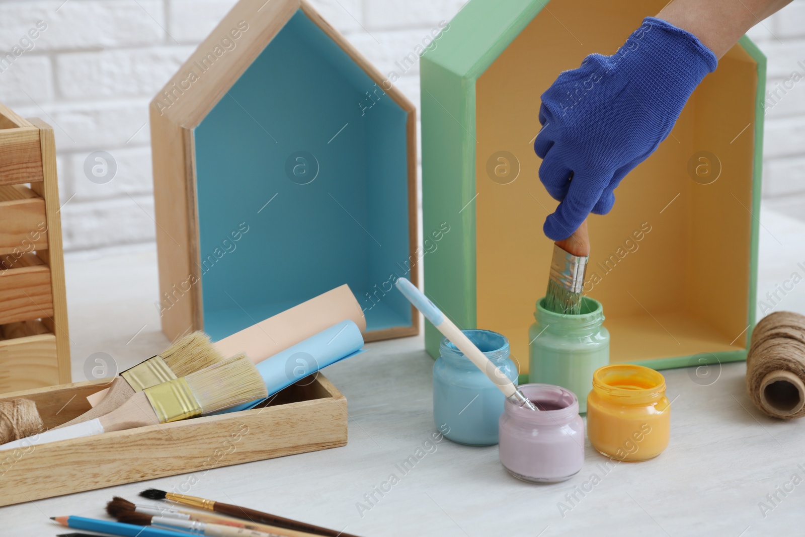 Photo of Decorator dipping brush into jar of green paint at white table, closeup