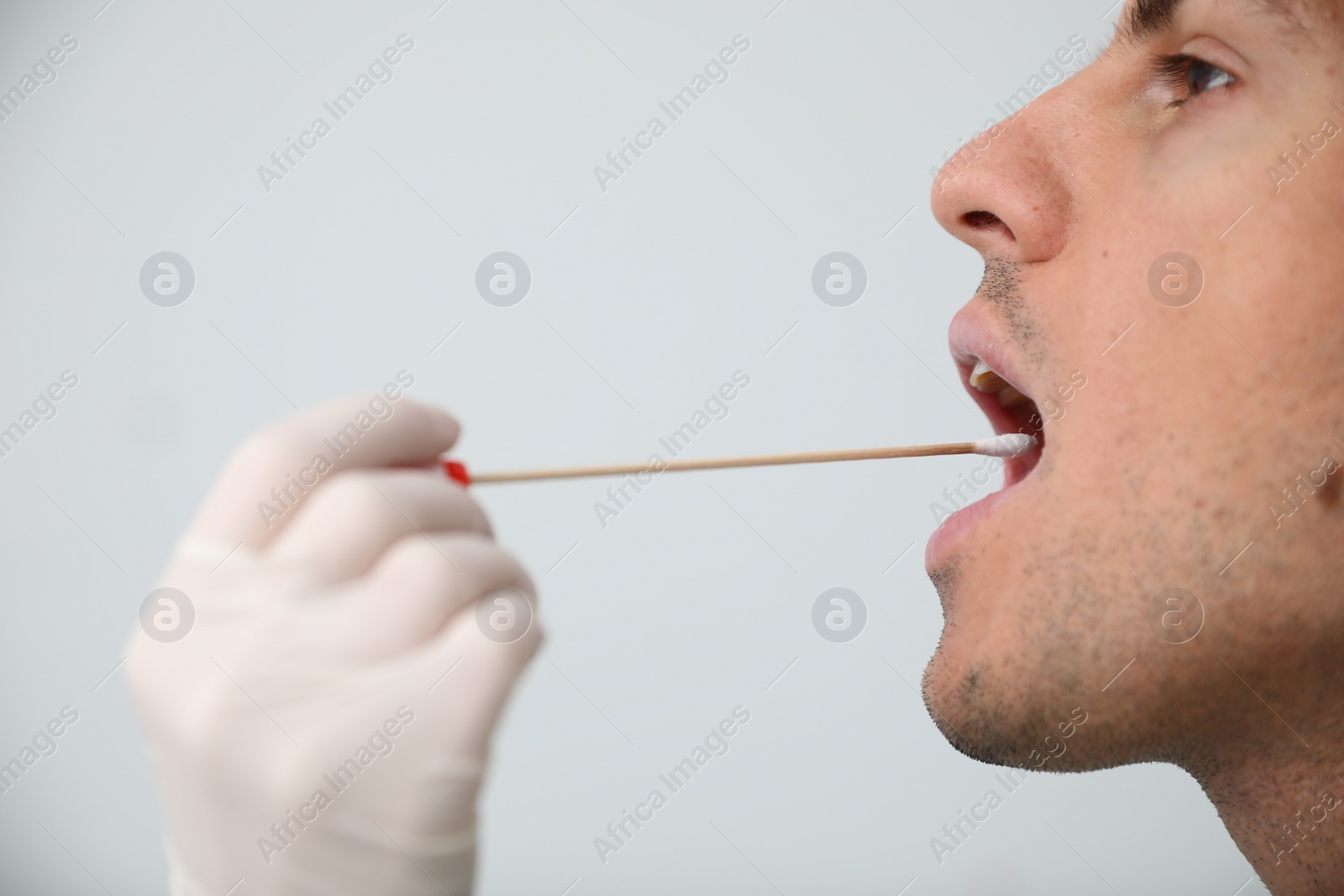 Photo of Doctor taking sample for DNA test from man on light background, closeup