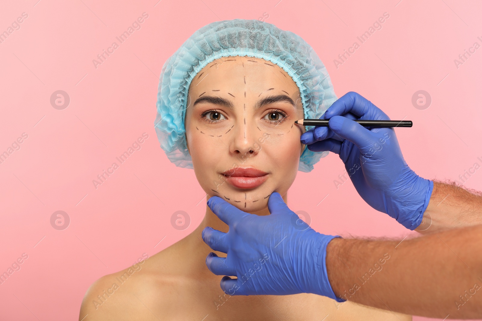 Photo of Doctor with pencil preparing patient for cosmetic surgery operation on pink background