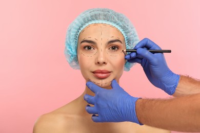 Photo of Doctor with pencil preparing patient for cosmetic surgery operation on pink background