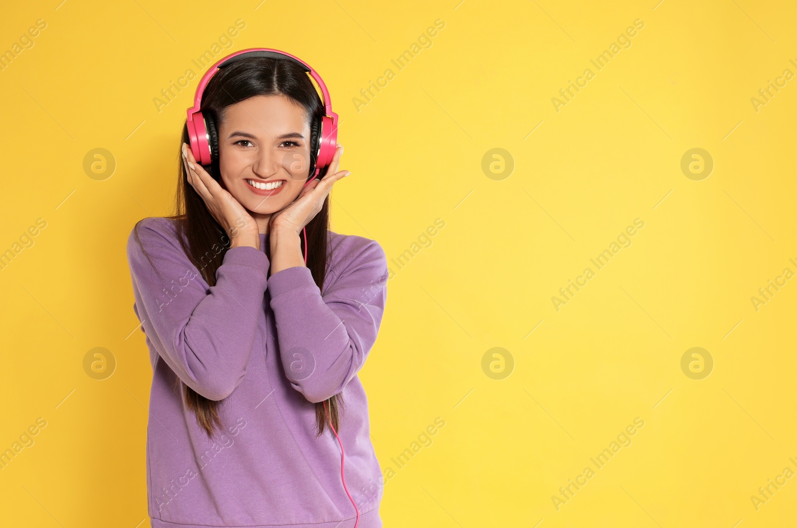 Photo of Attractive young woman enjoying music in headphones on color background. Space for text