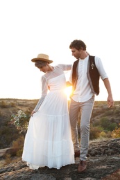 Happy newlyweds with beautiful field bouquet standing on rock at sunset