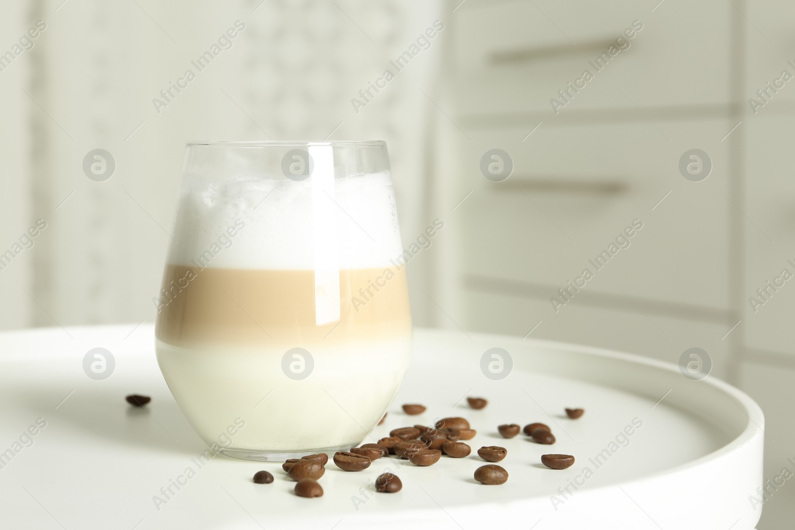 Photo of Delicious latte macchiato and coffee beans on white table indoors