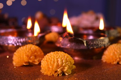 Photo of Diwali celebration. Diya lamps and chrysanthemum flowers on shiny table against blurred lights, closeup
