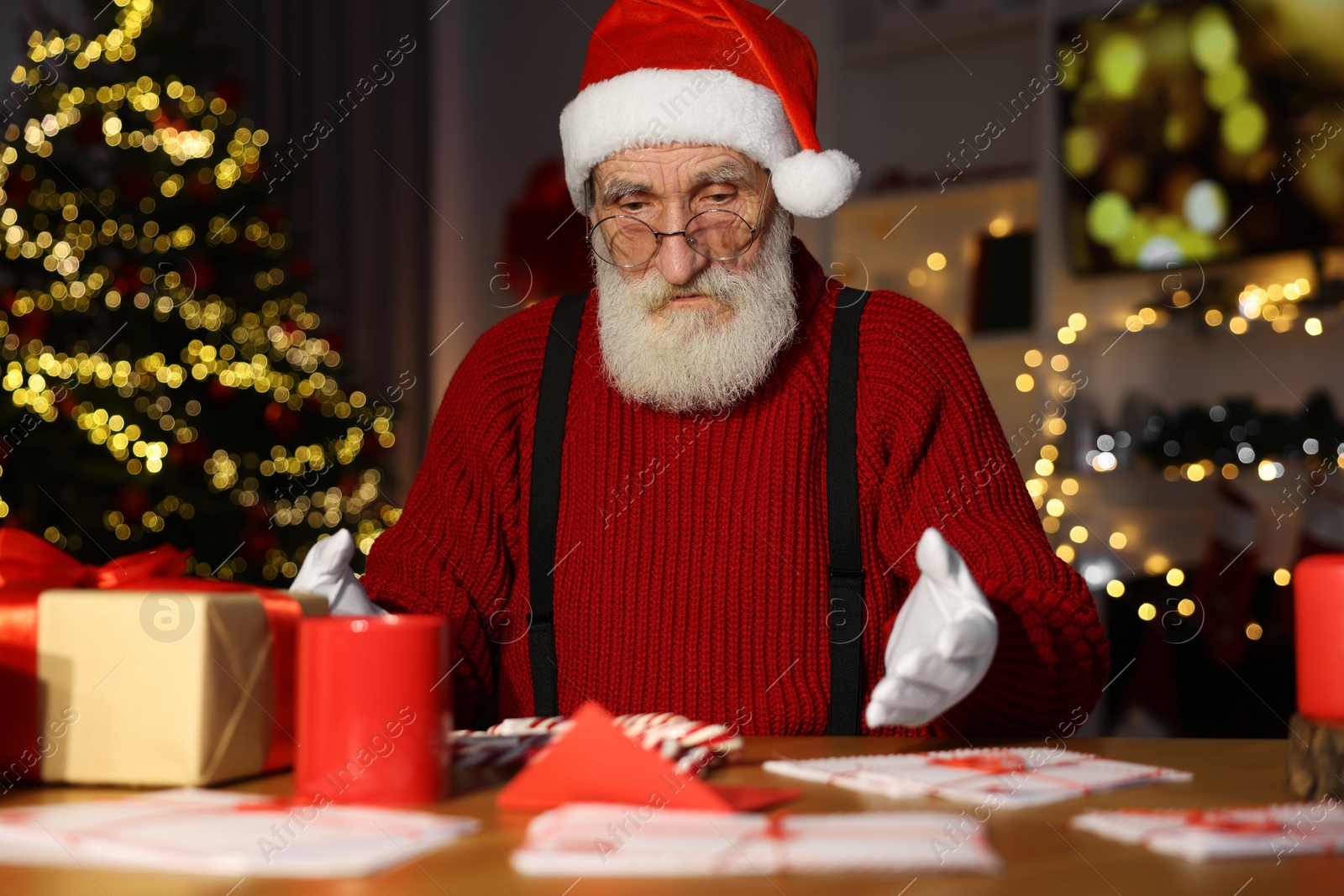 Photo of Santa Claus at his workplace. Letters and gift box on table in room with Christmas tree