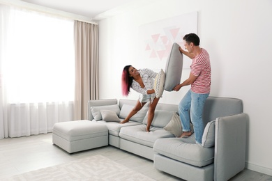 Photo of Happy couple having pillow fight on sofa at home