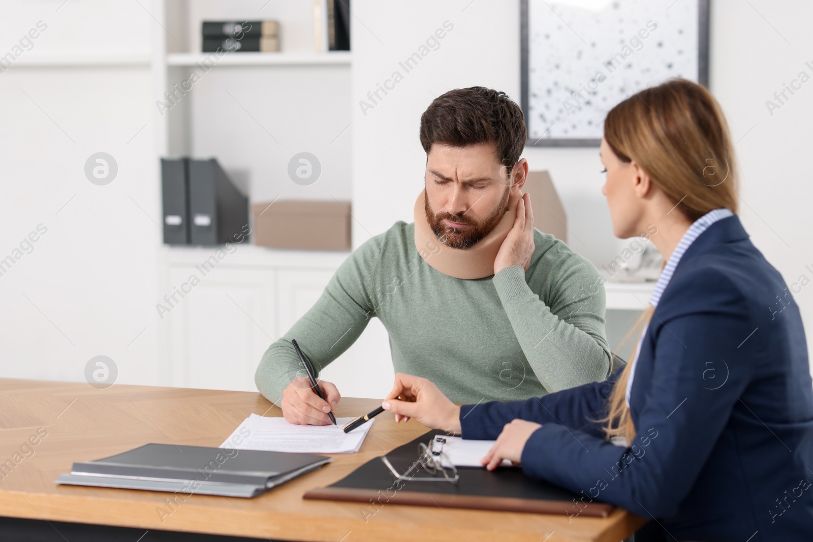 Photo of Injured man signing document in lawyer's office. Space for text