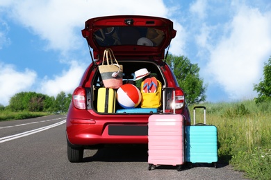 Suitcases near family car with open trunk full of luggage on highway