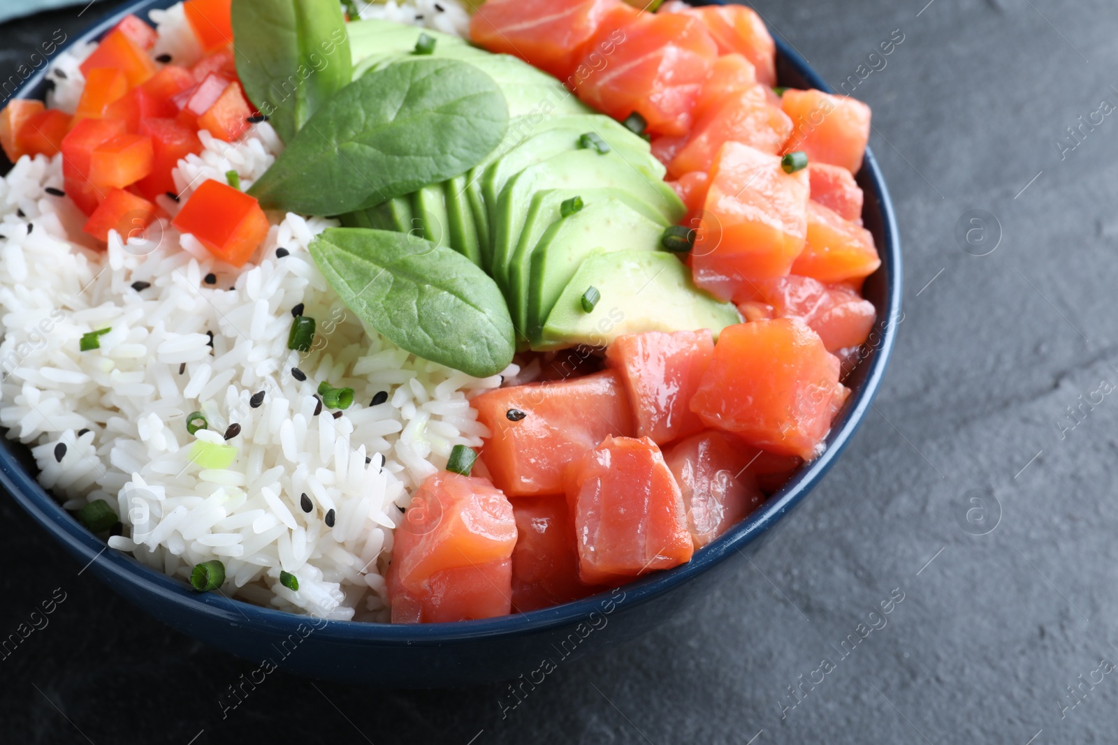 Photo of Delicious poke bowl with salmon, spinach and avocado on black table, closeup
