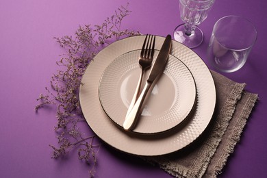 Photo of Stylish table setting. Plates, cutlery, glasses and floral decor on purple background, above view