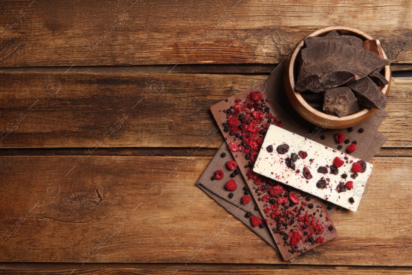 Photo of Different chocolate bars with freeze dried fruits on wooden table, flat lay. Space for text