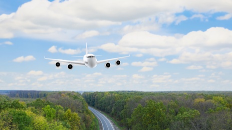 Modern airplane flying in cloudy sky over wood