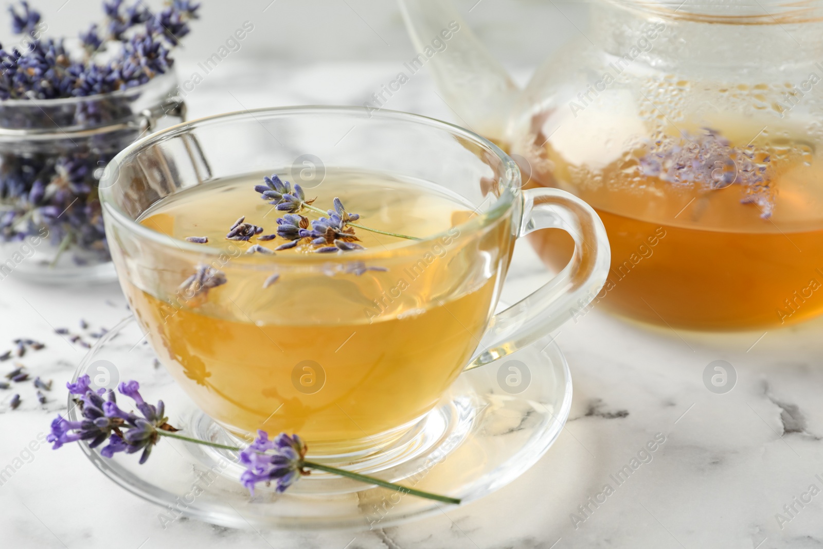 Photo of Fresh delicious tea with lavender and beautiful flowers on white marble table, closeup