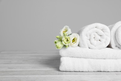 Photo of Soft white towels with flowers on wooden table against grey background, space for text