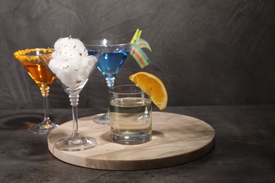 Tasty cotton candy cocktail and other alcoholic drinks in glasses on gray textured table, space for text