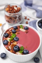 Bowl of delicious smoothie with fresh blueberries and granola on white tiled table, closeup