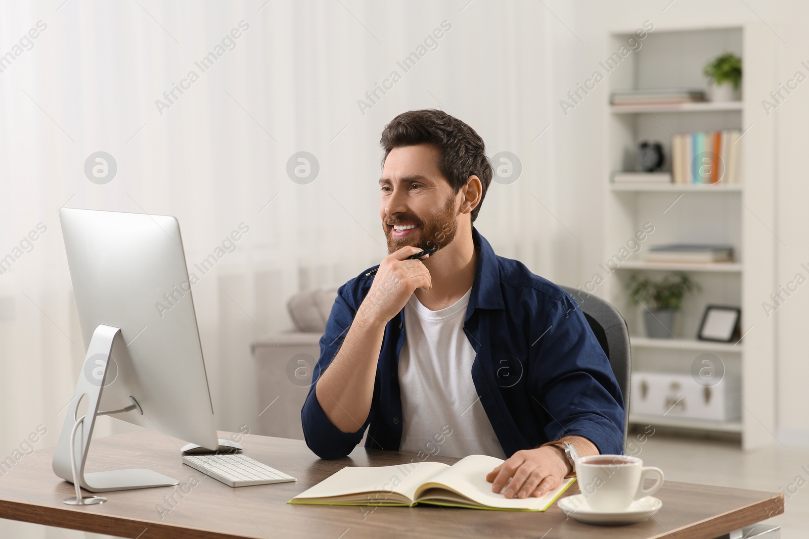 Photo of Home workplace. Happy man working with computer at wooden desk in room