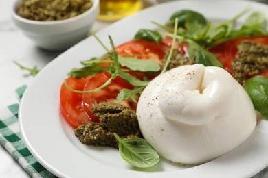 Photo of Delicious burrata salad with tomatoes, arugula and pesto sauce on table, closeup