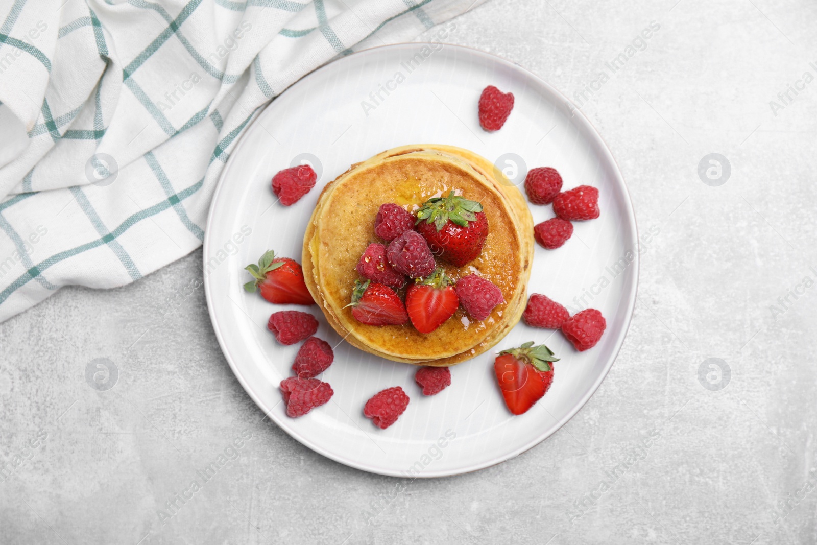 Photo of Tasty pancakes with fresh berries and honey on light grey table, top view