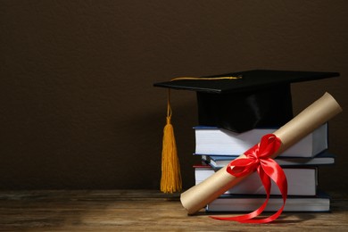 Graduation hat, books and diploma on wooden table against brown background, space for text