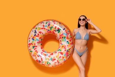 Photo of Young woman with stylish sunglasses holding inflatable ring against orange background