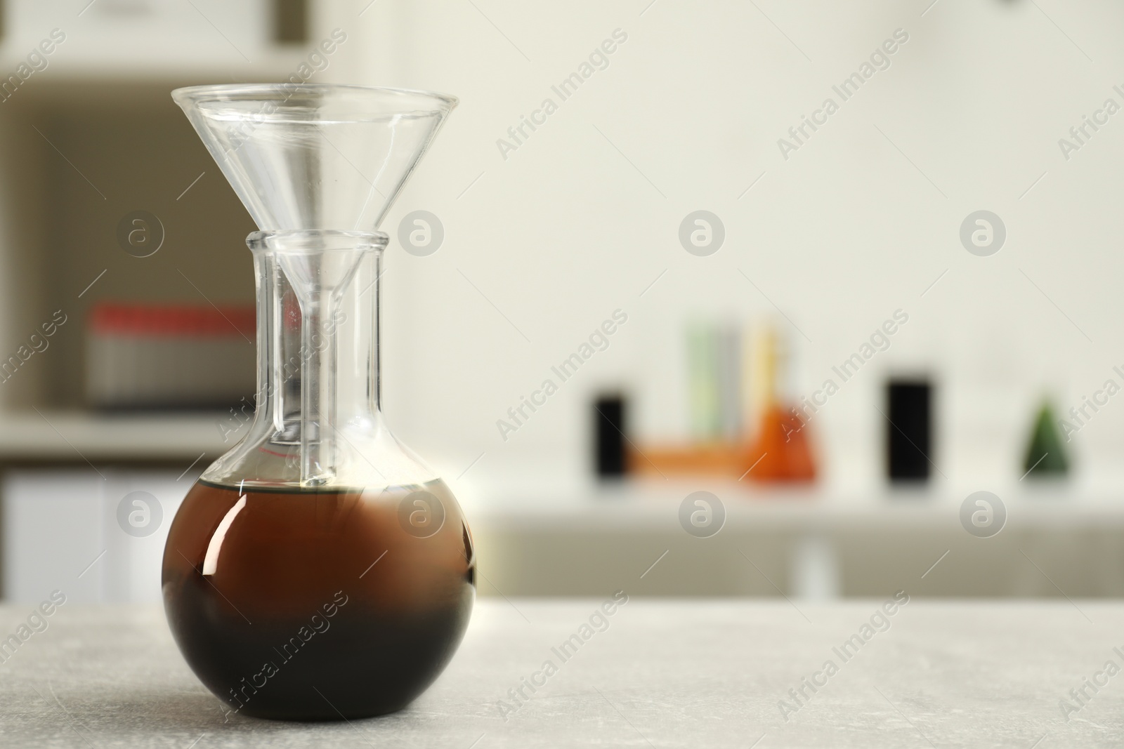 Photo of Flask with brown crude oil and filter funnel on light grey table, space for text