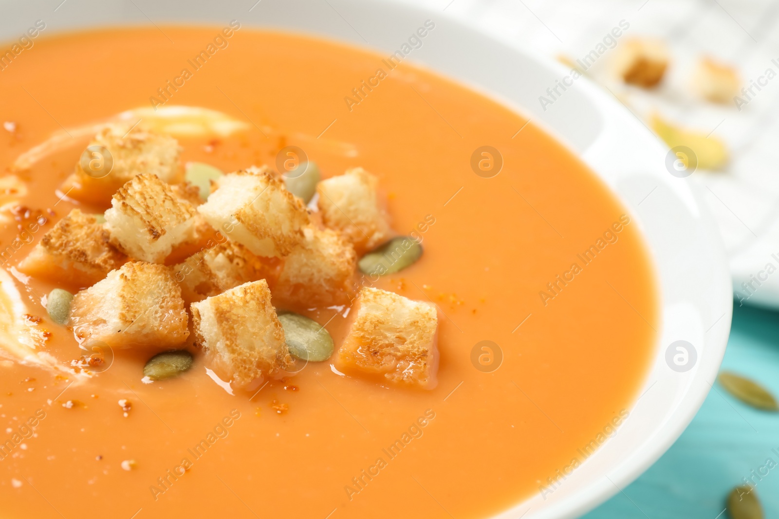 Photo of Tasty creamy pumpkin soup with croutons and seeds in bowl on table, closeup