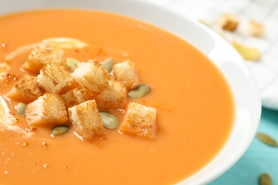 Tasty creamy pumpkin soup with croutons and seeds in bowl on table, closeup