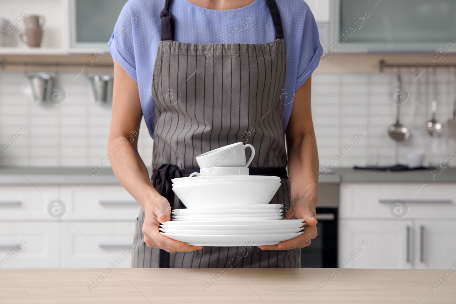 Photo of Woman with clean dishes and cups in kitchen, closeup