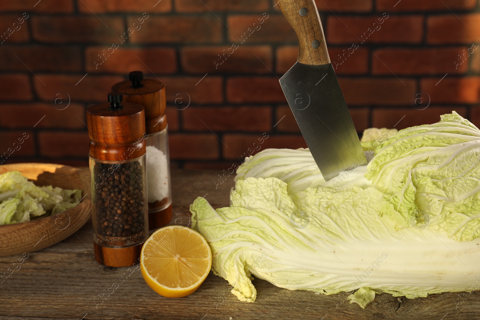 Photo of Fresh Chinese cabbage, knife, spices and lemon on wooden table