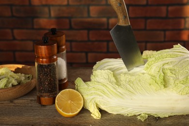 Photo of Fresh Chinese cabbage, knife, spices and lemon on wooden table