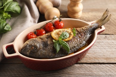 Delicious roasted dorado fish with tomatoes, basil and lemon on wooden table, closeup
