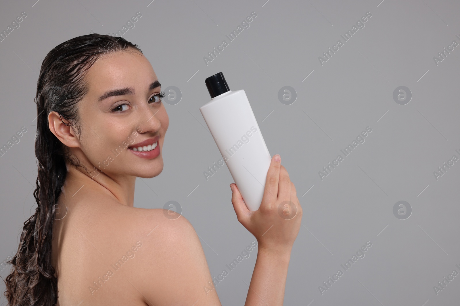 Photo of Washing hair. Portrait of beautiful happy woman with bottle on grey background. Space for text