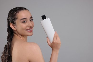 Washing hair. Portrait of beautiful happy woman with bottle on grey background. Space for text