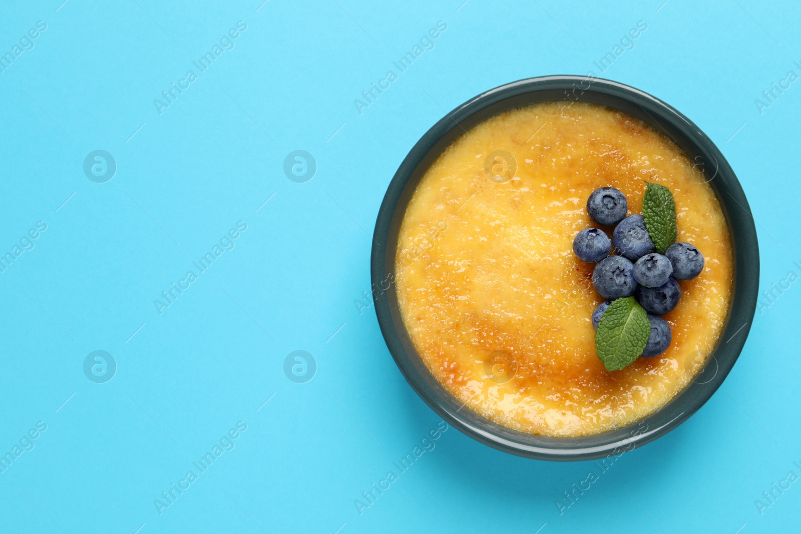 Photo of Delicious creme brulee with fresh blueberries and mint on light blue background, top view. Space for text