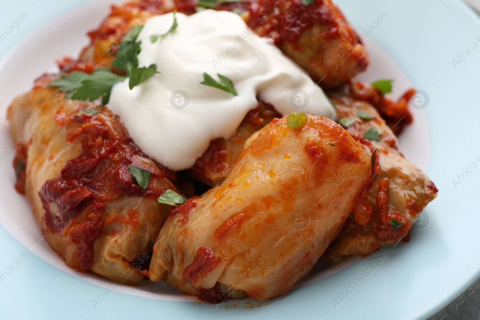 Photo of Delicious stuffed cabbage rolls served with sour cream on plate, closeup