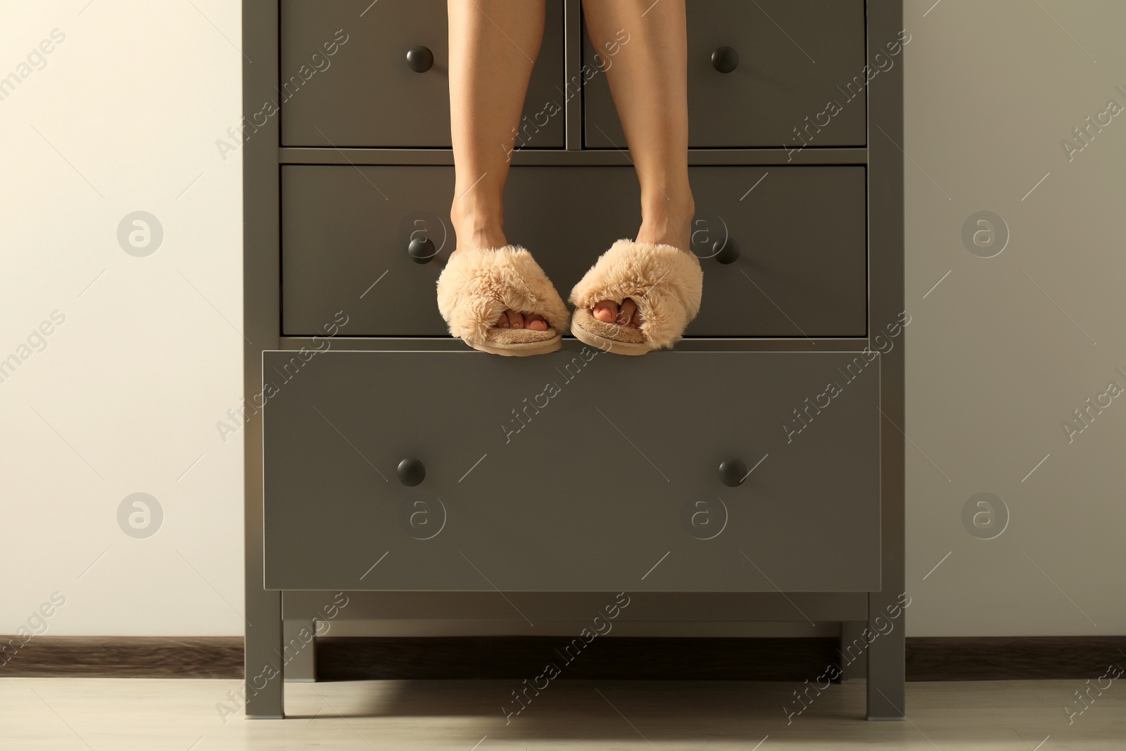 Photo of Woman in soft slippers sitting on chest of drawers, closeup