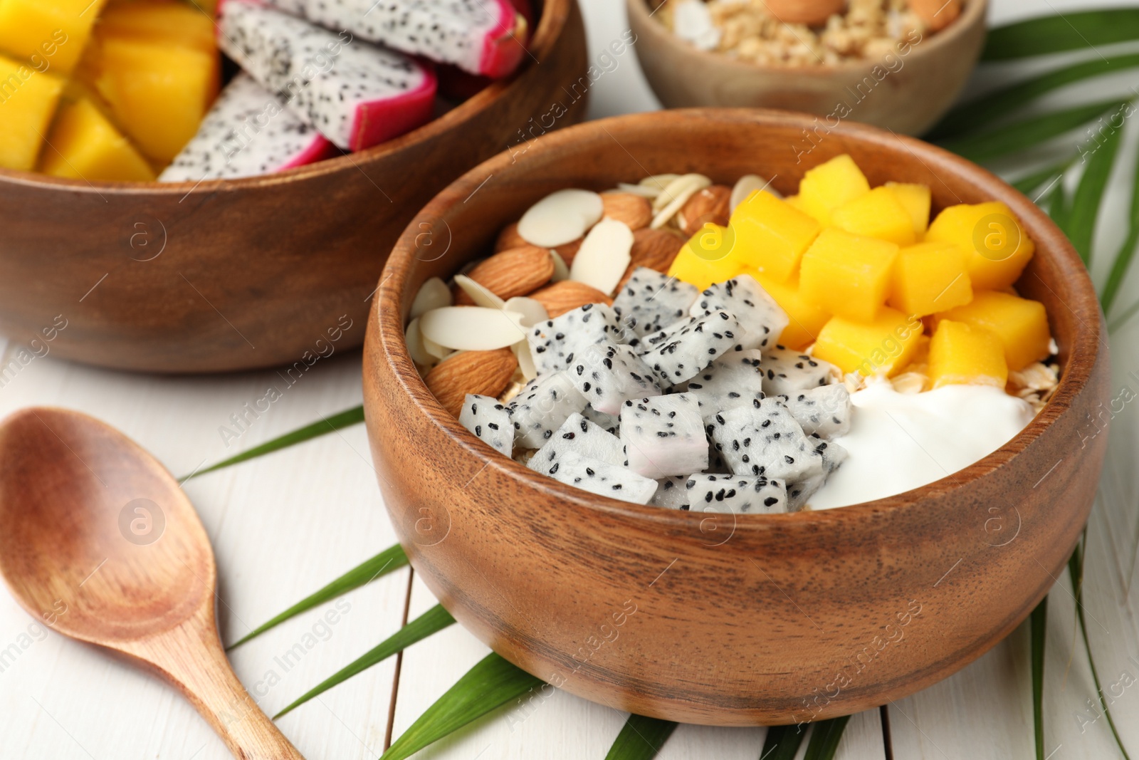 Photo of Bowl of granola with pitahaya, mango, almonds and yogurt on white wooden table