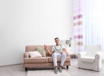 Happy young man operating air conditioner with remote control at home