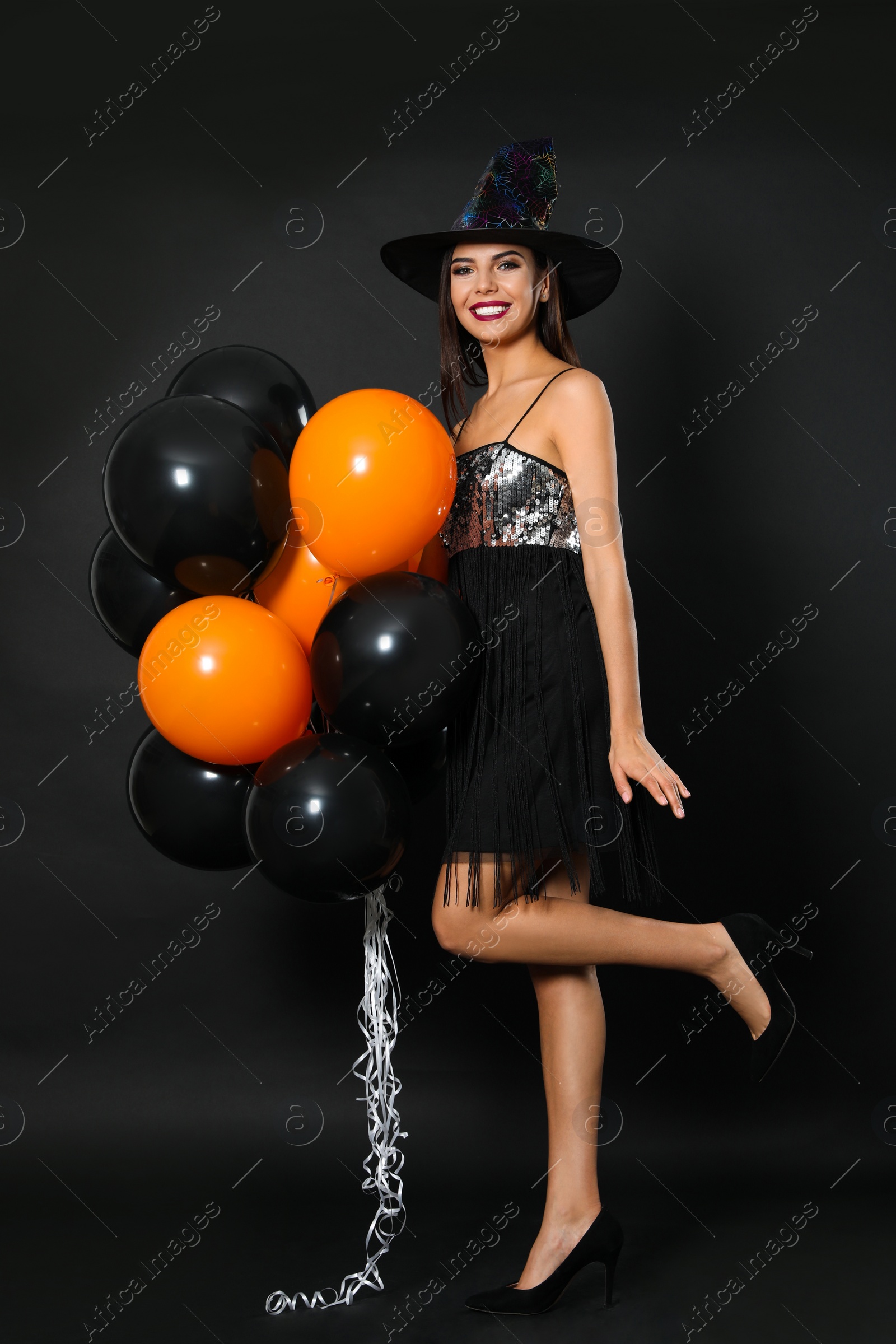 Photo of Beautiful woman wearing witch costume with balloons for Halloween party on black background