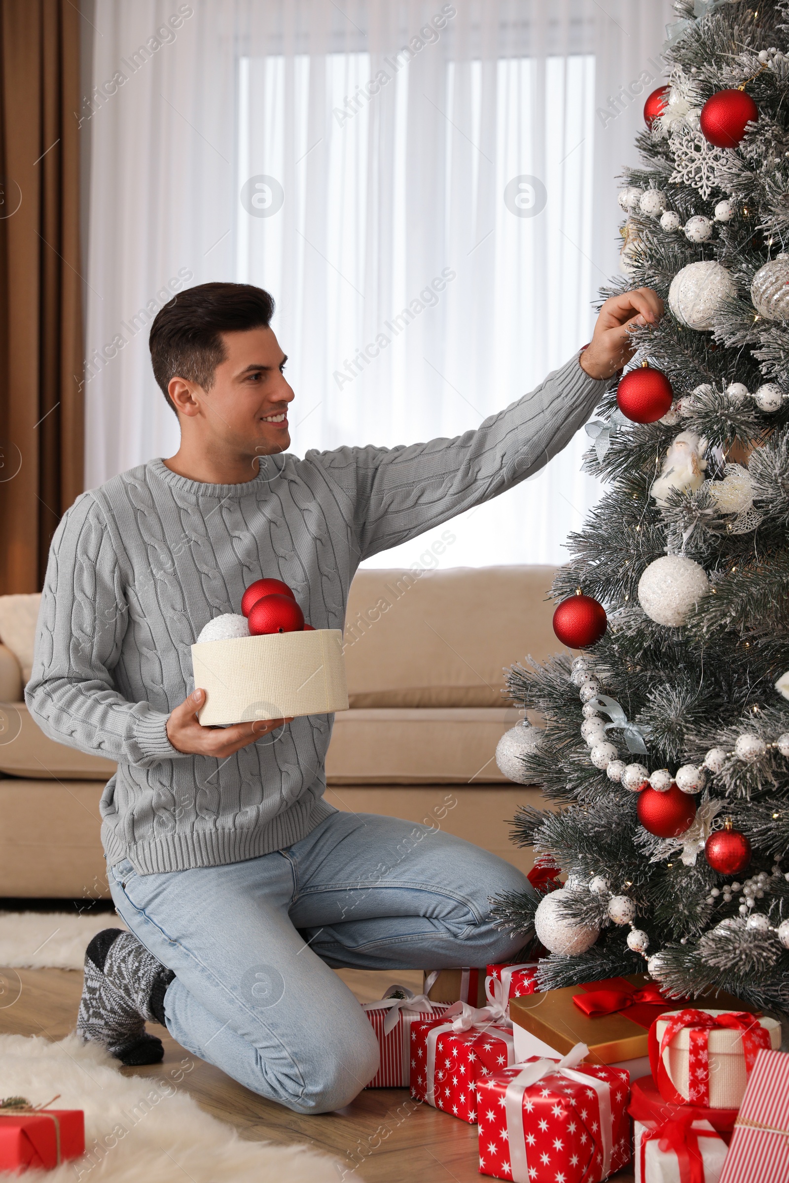 Photo of Handsome man decorating Christmas tree at home