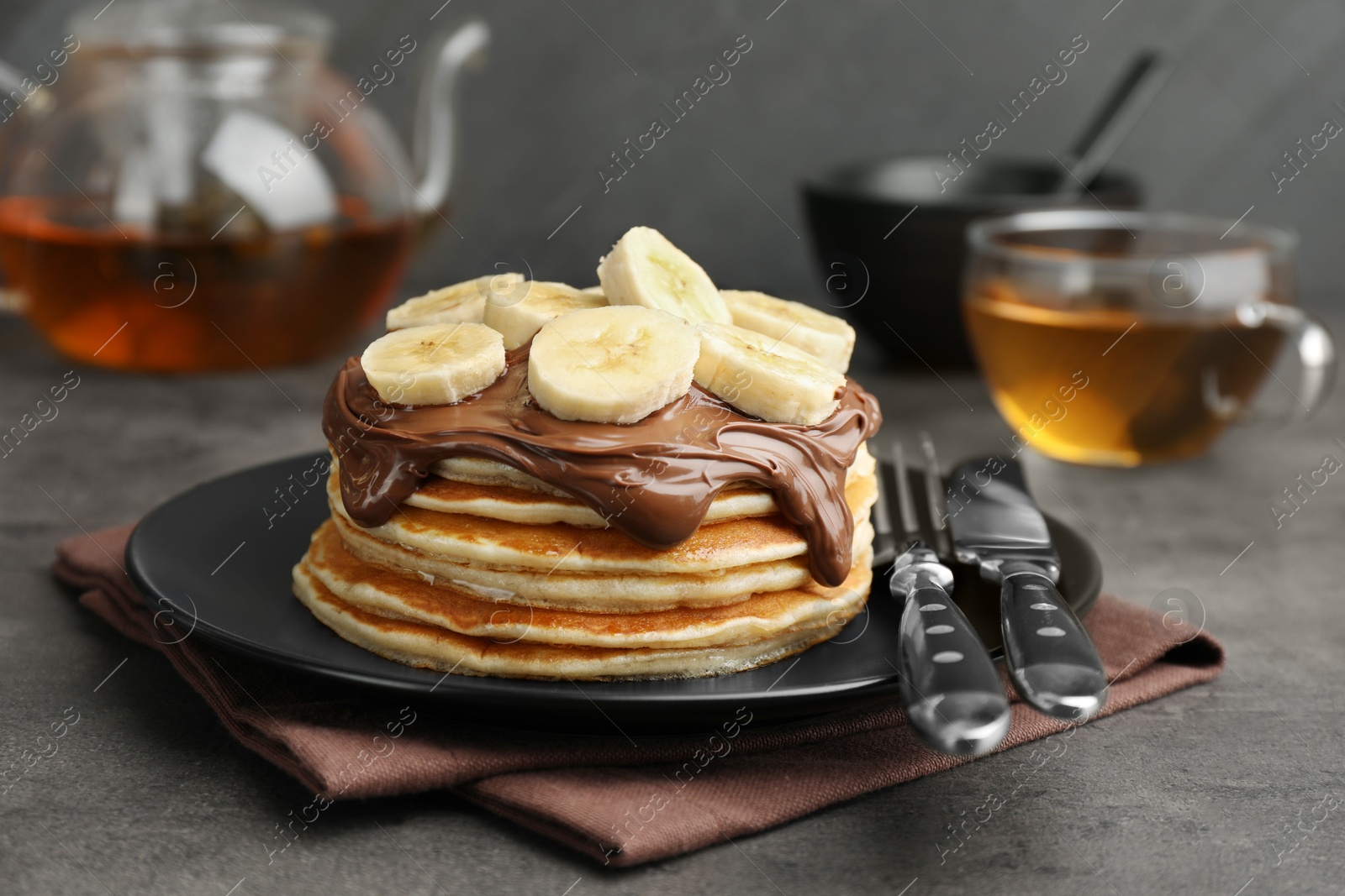 Photo of Tasty pancakes with chocolate spread and sliced banana served on gray table, closeup