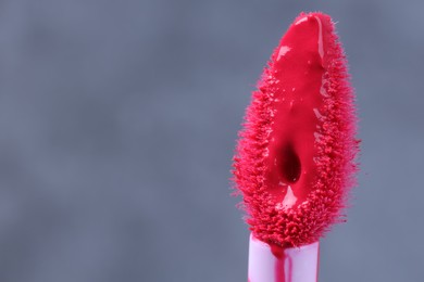 Photo of Brush with pink lip gloss on grey background, macro view. Space for text