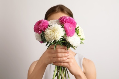 Photo of Woman holding beautiful aster flower bouquet against light background