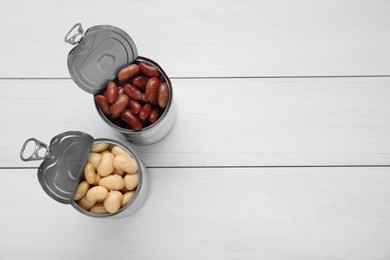 Photo of Tin cans with different canned kidney beans on white wooden table, flat lay. Space for text