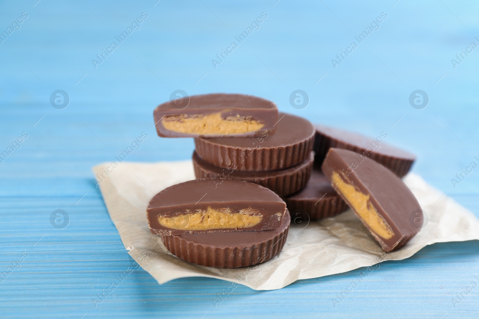 Photo of Cut and whole delicious peanut butter cups on light blue wooden table