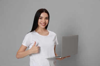 Young woman with modern laptop on light grey background