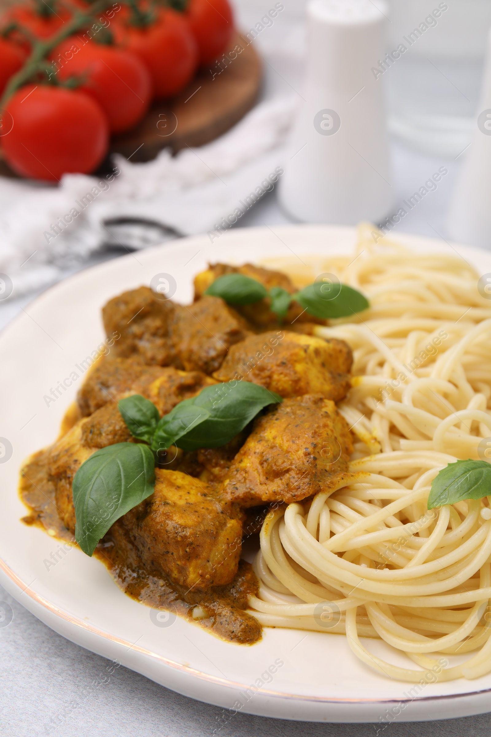 Photo of Delicious chicken, pasta with curry sauce and basil served on white table, closeup